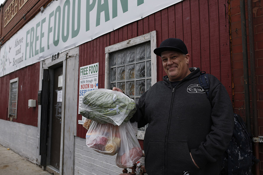 Un hombre sostiene bolsas de comida frente a una despensa de alimentos.