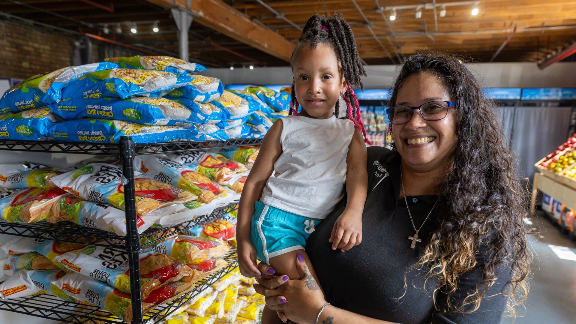 Woman holding a child in front of shelves of food at a pantry